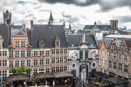 Ghent, Belgium - September 23, 2018: Seen from Gent Castle tower. Gray statue decorated gate to historic fish market among red brick facades of historic houses now restaurants. Cloudscape and towers on horizon.のeditorial素材
