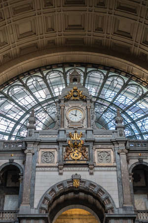 Antwerp, Belgium - September 24, 2018: Gray, beige, brown Monumental hall and arch over stairway to train hall at Antwerpen Centraal railway station. closeup of clock and Belgian coat of arms.のeditorial素材