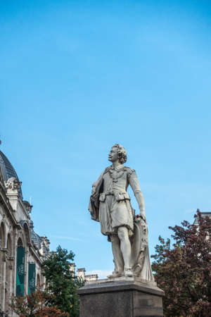 Antwerp, Belgium - September 24, 2018: Gray statue of Sir Anthony Van Dyck Flemish Painter against blue sky at Meir and Leysstraat link. Facades and some green foliage.のeditorial素材