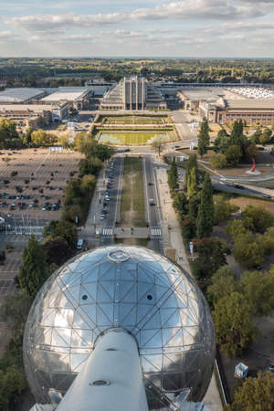 Brussels, Belgium - September 25, 2018: The historic world expo halls shot from top of the Atomium monument. Green belt and cloudy sky on horizon. One of the Atomium spheres up front.のeditorial素材