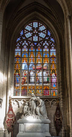 Brussels, Belgium - September 26, 2018: Stained Glass Window of Cathedral of Saint Michael and Saint Gudula. White stone tomb monument in front.のeditorial素材