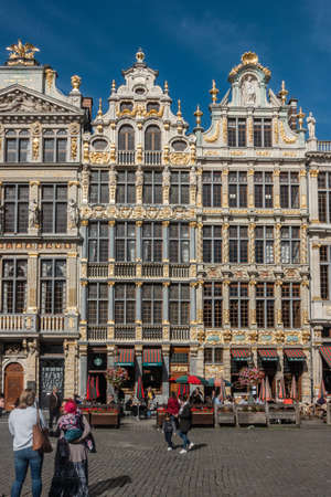 Brussels, Belgium - September 26, 2018: Three brown stone facades with golden decorations and statues on Grand Place against blue sky. People walking on square.のeditorial素材