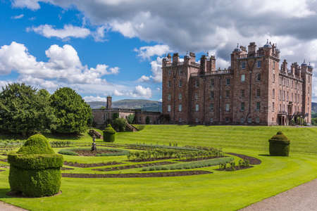 Holm of Drumlanrig, Scotland, UK - June 18, 2012: Free standing pink sand stone Drumlanrig Castle on its higher plateau under cloudy sky. Part of the extensive green garden up front.のeditorial素材