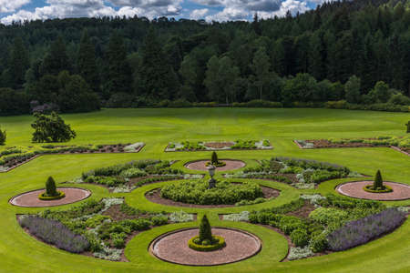 Holm of Drumlanrig, Scotland, UK - June 18, 2012: Green garden of Drumlanrig Castle under cloudy sky. Dark green forest at borders.のeditorial素材
