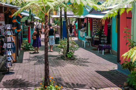 Kuranda, Queensland, Australia - December 4, 2009: Central walkway and booths at Kuranda Rainforest Market. Colorful clothes, souvenirs and craft shops. People and green foliage.のeditorial素材