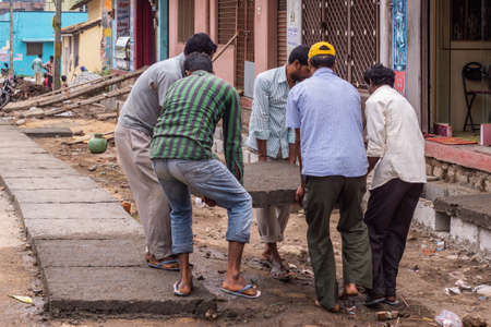 Belur, Karnataka, India - November 2, 2013: Five guys handle heavy concrete plate lying is down to cover a sewer line. Street scene with people.のeditorial素材