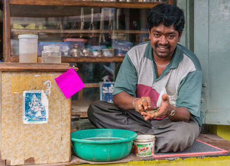 Belur, Karnataka, India - November 2, 2013: Closeup of jeweler man cleaning golden jewelry in soapy basin in front of his shop. Goddess Saraswati picture nearby.のeditorial素材