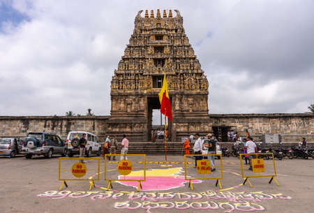 Belur, Karnataka, India - November 2, 2013: Brown stone Gopuram of main entrance seen from street against white cloudy sky. Karnataka Rajyotsava sign and flag up front. People and cars.のeditorial素材