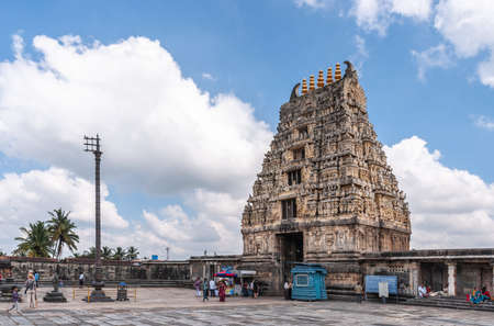 Belur, Karnataka, India - November 2, 2013: Brown stone Gopuram of main entrance seen from inside temple against blue sky. Booths, signs and people. Ceremonial flag pole against white cloud.のeditorial素材