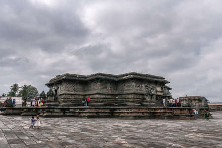 Belur, Karnataka, India - November 2, 2013: Chennakeshava Temple. Courtyard shows Northeast corner of dark brown stone Kesava temple building under gray cloudscape. People add color.のeditorial素材