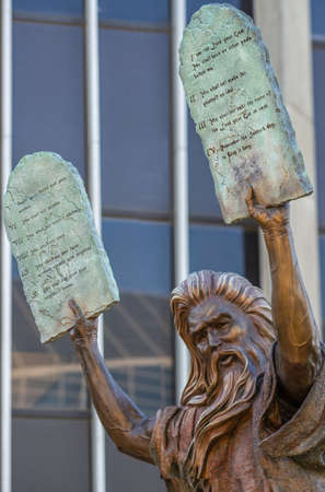 Garden Grove, California, USA - December 13, 2018: Crystal Christ Cathedral. Closeup of Bronze statue of Moses putting the ten commandments of two tables in the air. Some green foliage, facade of Tower of Hope.のeditorial素材