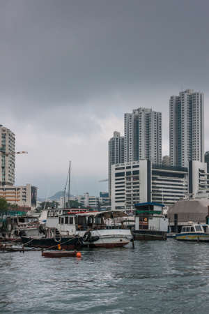 Hong Kong, China  - May 12, 2010: Dilapidated houseboats floating in central harbor with tall highrise buildings in back under heavy rainy cloudscape.のeditorial素材