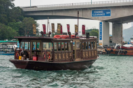 Hong Kong, China - May 12, 2010: Brown and golden decorated tourist vessel travels in the old central harbor passing under Eastern Harbour bridge. Silver sky and greenish water.のeditorial素材