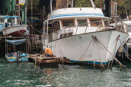Hong Kong, China  - May 12, 2010: Man works to restore a white yacht and houseboat docked along the shore of the inner harbor. Other small boats and stuff around.のeditorial素材