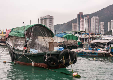 Hong Kong, China  - May 12, 2010: Closeup of Green and black wooden old houseboat in harbor. Sloops around, hill and tall highrise buildings on shore in background. All under silver sky.のeditorial素材