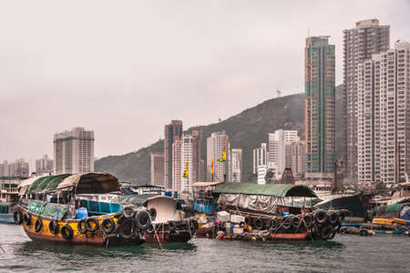 Hong Kong, China  - May 12, 2010: Very tall gray and green highrise buildings behind green, yellow and red ferry sampans in harbor under silver sky.のeditorial素材