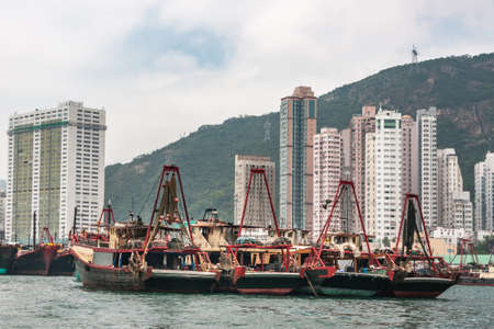 Hong Kong, China  - May 12, 2010: Four black and red fishing vessels docked in  harbor with white tall apartment buildings on shore. Silver sky over green hill.のeditorial素材