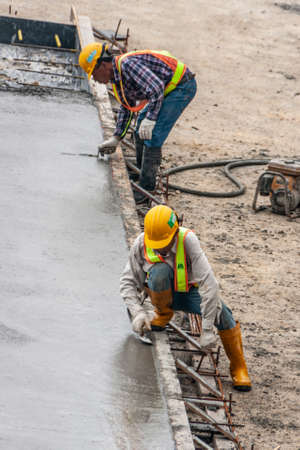 Hong Kong Island, China  - May 14, 2010: Two Construction workers at second International Finance Center flatten manually wet concrete.のeditorial素材
