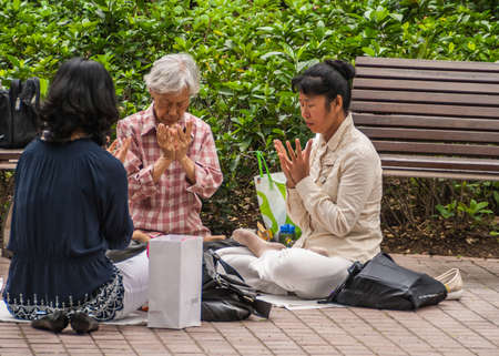 Hong Kong, China  - May 13, 2010: Kowloon Park, Tsim Sha Tsui. Three women take time to meditatie and pray sitting on the ground in the park. Shopping bags beside them. Green background.のeditorial素材