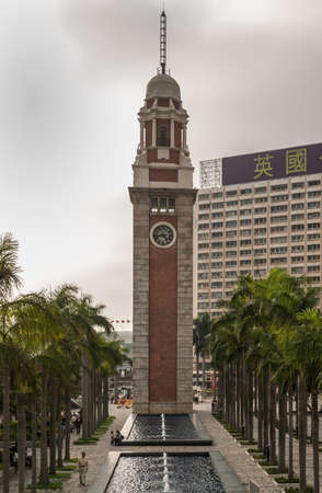Hong Kong, China  - May 12, 2010: Former Kowloon-Canton Railway Clock Tower against rain cloudy sky. Green palm trees at bottom with reflection pool and people.のeditorial素材