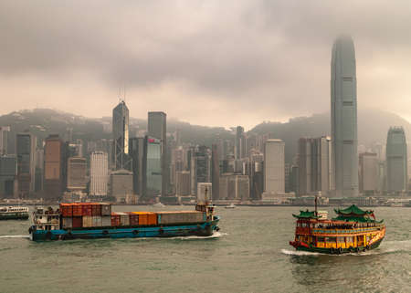 Hong Kong Island, China  - May 12, 2010: Skyline with International Finance Center and more under dark foggy sky,. Container ship and Watertours sampan-style river cruise boat in front on Victoria Harbour.のeditorial素材