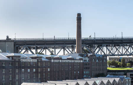Sydney, Australia - February 12, 2019: Historic harbor warehouses with tall chimney sports Metcalfe Bond advertisement on facade. At foot of Harbour bridge.のeditorial素材