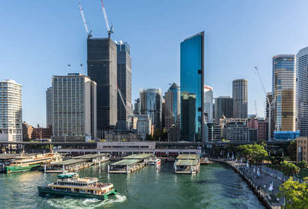 Sydney, Australia - February 12, 2019: Western side of ferry terminal and Circular Quay Railway Station plus skyline in back. Highrises under construction with cranes. Evening shot with light blue sky.のeditorial素材
