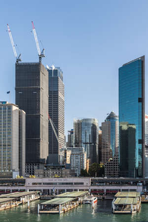 Sydney, Australia - Sydney, Australia - February 12, 2019: Part of ferry terminal and Circular Quay Railway Station plus skyline in back. Highrises under construction with cranes. Evening shot with light blue sky.のeditorial素材