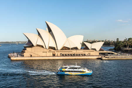 Sydney, Australia - February 12, 2019: Side view of the Opera House during sunset, with Whale Watching cruise vessel. Blue sky and water. Horizon is shore of bay.のeditorial素材