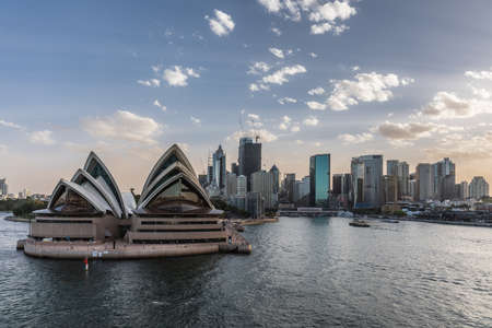 Sydney, Australia - February 12, 2019: North side of the Opera House and city skyline. Light Blue sky and gray water. Circular bay ferry terminal and railway station. Boats in water.のeditorial素材