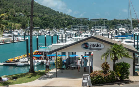 Hamilton Island, Australia - February 16, 2019: Jetski rental business on side of yacht harbor in the marina. Plenty of white boats on azure water. Back is mountain of green foliage against blue sky.のeditorial素材