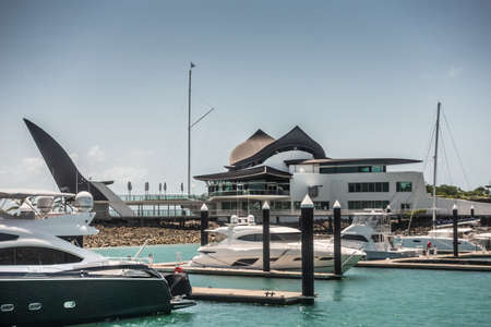 Hamilton Island, Australia - February 16, 2019: Black and white Iconic Yacht Club House, set in marina with white yachts, under blue sky.のeditorial素材
