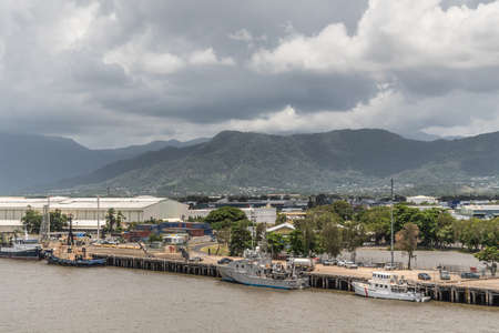 Cairns, Australia - February 17, 2019: Industrial part of the harbor with warehouses, containers and smaller ships along Chinaman Creek. Kuranda National Park mountains under cloudscape.のeditorial素材