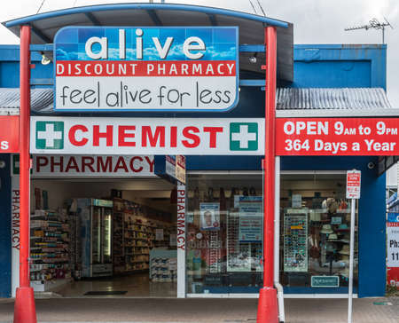 Cairns, Australia - February 17, 2019: Pharmacy and Chemist business in Abbott Street features blue and red advertisements. Open doors and gray skies.のeditorial素材