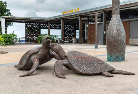 Cairns, Australia - February 17, 2019: Metal sea turtle statues on the wharf celebrating seasonal phoenomenom of mating by Dennis Nona. Back is Wharf One Cafe entrance. Cloudscape and green foliage.のeditorial素材