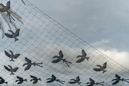Cairns, Australia - February 17, 2019: Net of birds artwork by Dennis Nona on the wharf. Black figures against gray cloudy sky.のeditorial素材