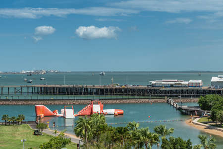 Darwin Australia - February 22, 2019: Big Buoy Water Park with red and white water slide in center of harbour showing boats, warehouses and green zone under blue sky.のeditorial素材