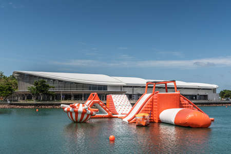 Darwin Australia - February 22, 2019: Big Buoy Water Park with red and white water slide in center of harbour in front of Convention Centre under blue sky.のeditorial素材