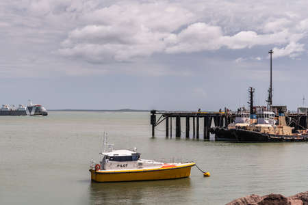 Darwin Australia - February 22, 2019: Closeup of anchored pilot boat with tugboats docked in back under blue sky with white cloudscape and gray seawater.のeditorial素材