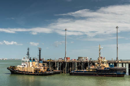Darwin Australia - February 22, 2019: Closeup of three tugboatd docked along wharf in the harbour under blue sky with white cloudscape upon greenish sea water.のeditorial素材