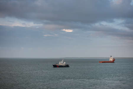 Darwin Australia - February 22, 2019: Two ships sail in opposite direction in the large harbour bay under evening cloudscape. Horizon is small line of land.のeditorial素材