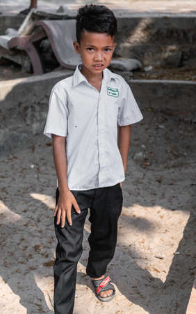 Sihanoukville, Cambodia - March 15, 2019: Closeup of young Cambodian boy with white shirt and black pants on flip-flops in the dirt near Phsar Leu market.のeditorial素材