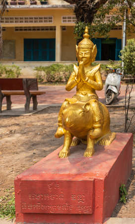 Sihanoukville, Cambodia - March 15, 2019: Phsar Leu Elementary School. Closeup portrait of golden statue of Year of Rat, with Buddhist figure on animal. Red pedestal, green foliage.のeditorial素材
