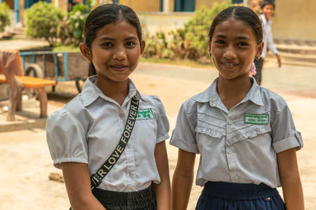 Sihanoukville, Cambodia - March 15, 2019: Phsar Leu Elementary School. Closeup portrait of two young school girls in white shirt and blue skirt. Smiling.のeditorial素材