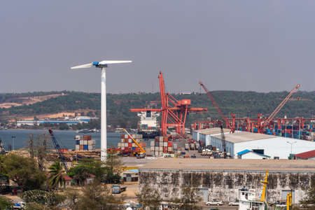 Sihanoukville, Cambodia - March 15, 2019: Container terminal of Sihanoukville Autonomous Port under blue sky. Red cranes and white warehouses. Green hills on horizon.のeditorial素材