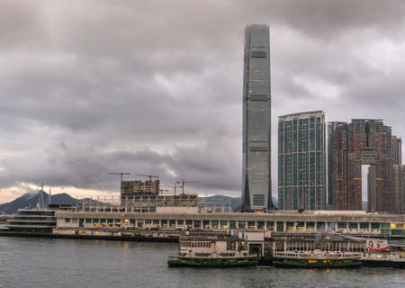 Hong Kong, China - March 7, 2019: Very early morning under dark rainy sky. Kowloon skyline at Cruise and Ferry terminal at Victoria Harbour with International Commerce Center tower.のeditorial素材