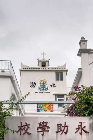 Hong Kong, China - March 7, 2019: Tai O Fishing village. White building is Wing Choh Primary school, a Christian enterprise, under silver sky. One poster praising God adds color.のeditorial素材