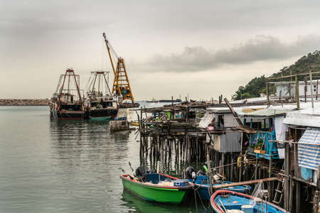 Hong Kong, China - March 7, 2019: Tai O Fishing village. Modern larger fishing vessels docked in port and small sloops under cloudscape with yellowish horizon over sea.のeditorial素材