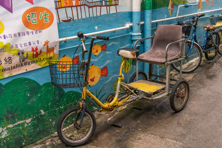 Hong Kong, China - March 7, 2019: Tai O Fishing village. Tricycle one-guest taxi parked in street, for family use to transport elderly disabled family member. Yellow and brown vehicle against blue wall.のeditorial素材