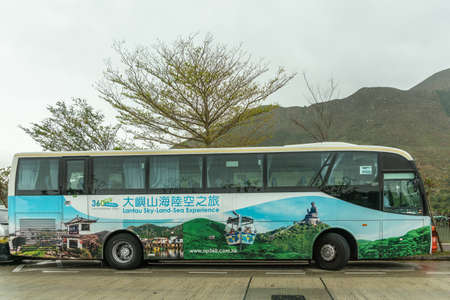 Hong Kong, China - March 7, 2019: Tai O Fishing village. Large tourist bus parked outside the village is painted with views of famous Lantau islands. Back is green hill. silver sky.のeditorial素材